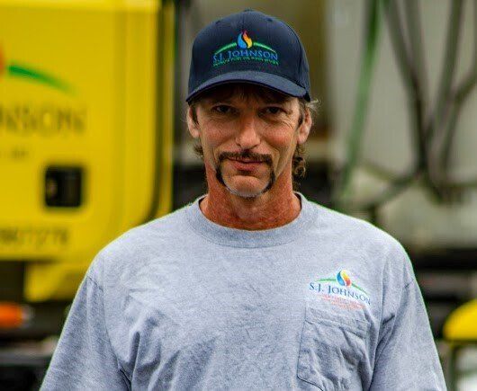 A man wearing a hat and a gray shirt is standing in front of a yellow truck.