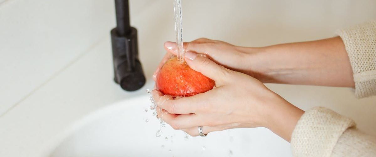 a woman is washing an apple in a sink using water softened filtered water