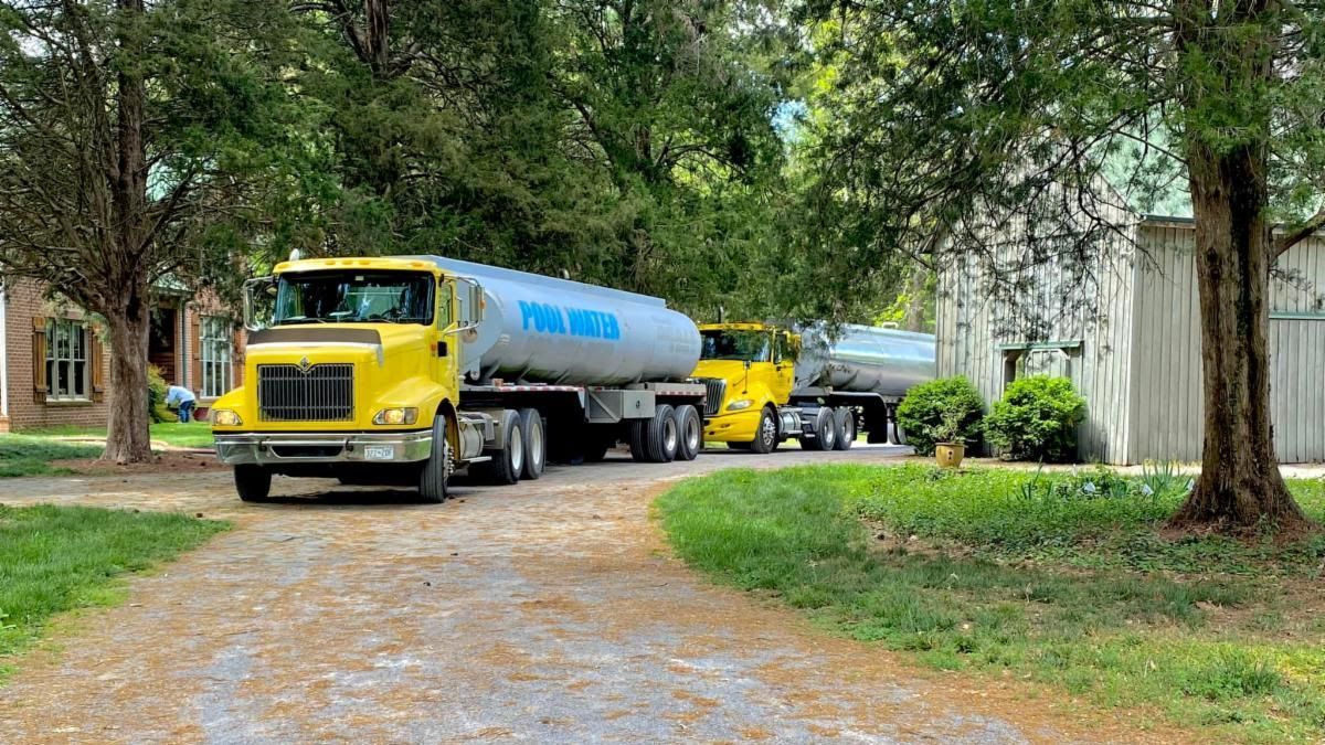 Two tanker trucks are parked in a driveway next to a house.