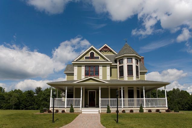 A large green house with a large porch on a sunny day.