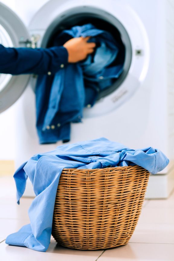 A person is putting blue clothes into a washing machine