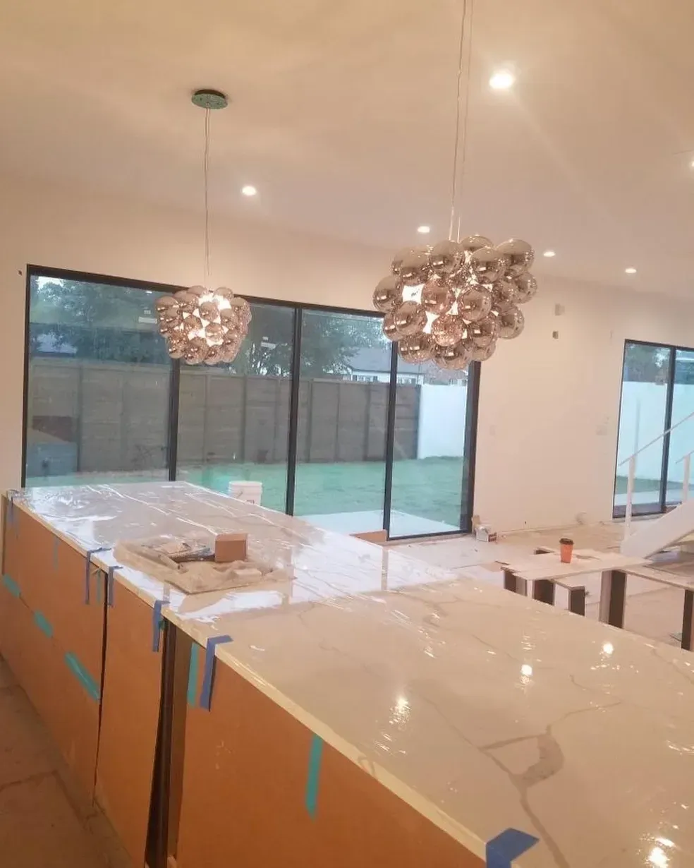 Two modern pendant lights hang over a kitchen island, with glass bubble-like fixtures. A large glass sliding door overlooks a backyard.
