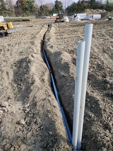 Construction site trench with installed conduit and upright pipes.
