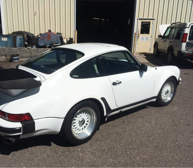 White Porsche 911 sports car parked outside a garage, with a black spoiler and black side stripe | Ken's Import Service