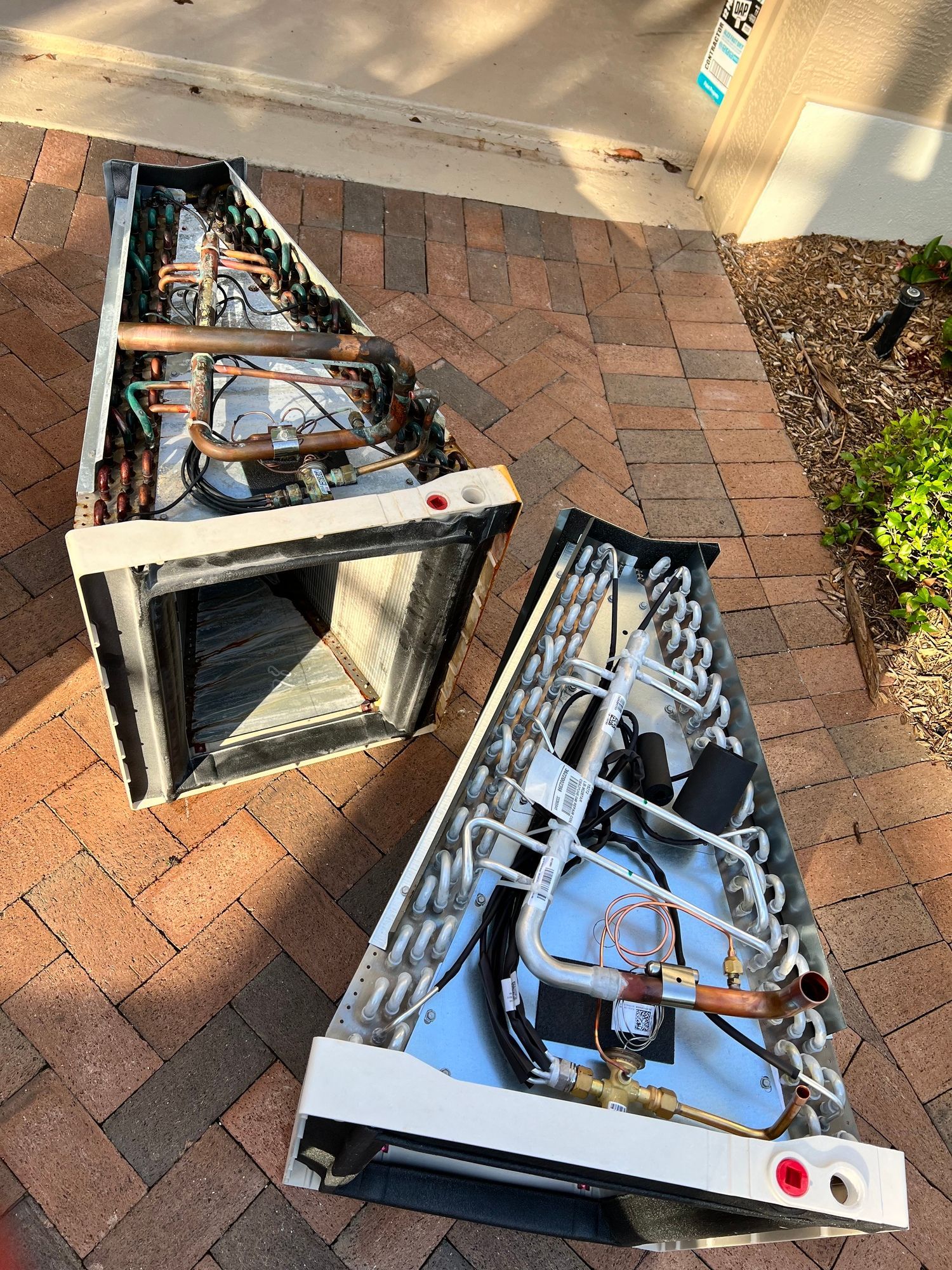 two air conditioners are sitting on top of each other on a brick sidewalk .