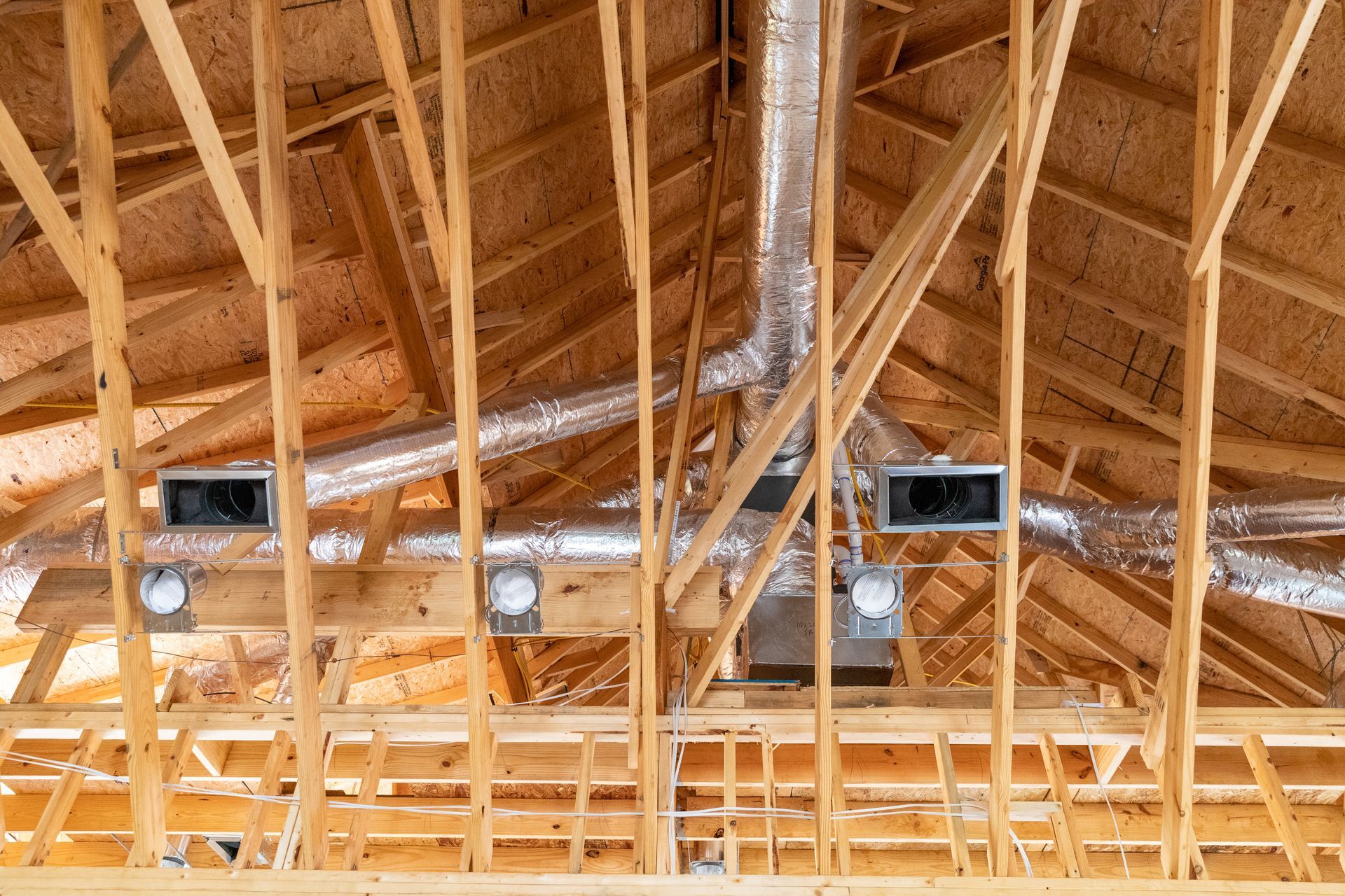 the ceiling of a house under construction with wooden beams and ducts .