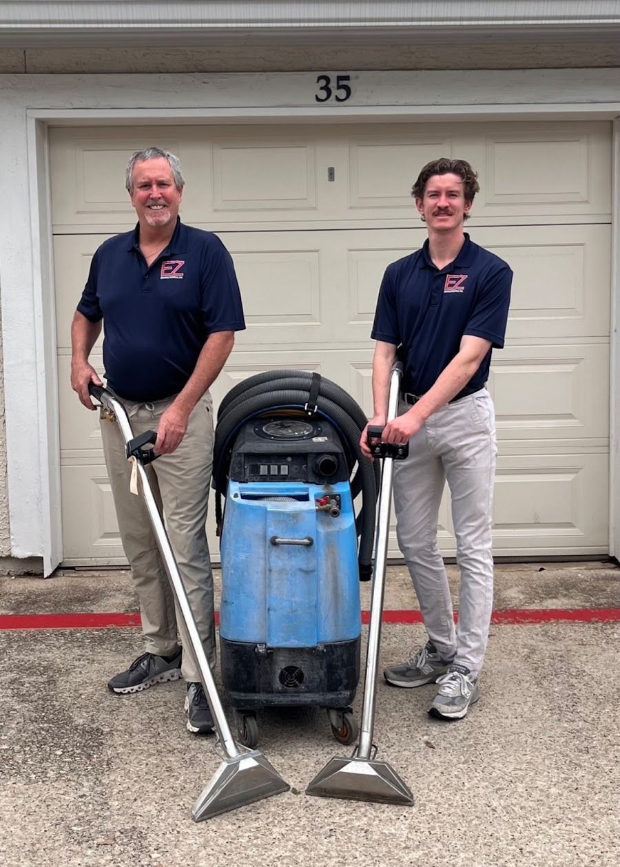Two men are standing next to each other holding vacuum cleaners in front of a garage door.