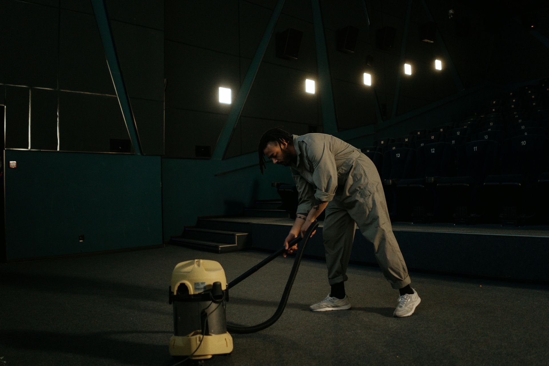 A man is using a vacuum cleaner to clean the floor in a dark room.