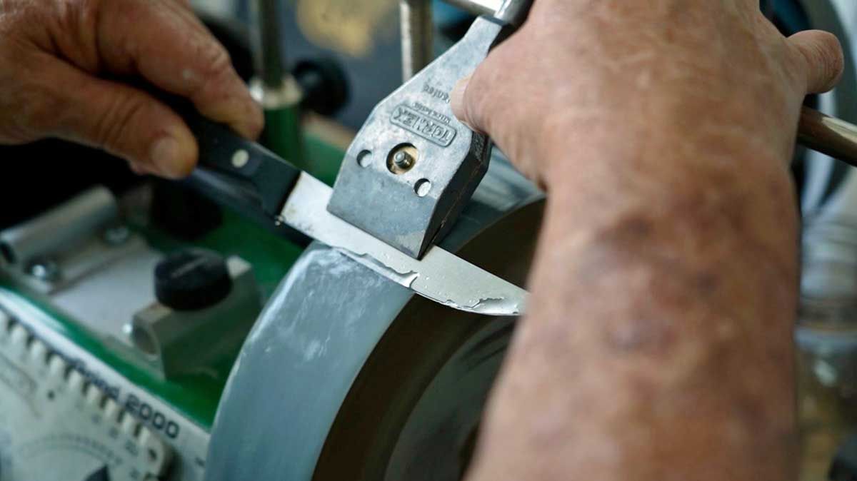A pair of hands sharpening a knife using the water honing machine.