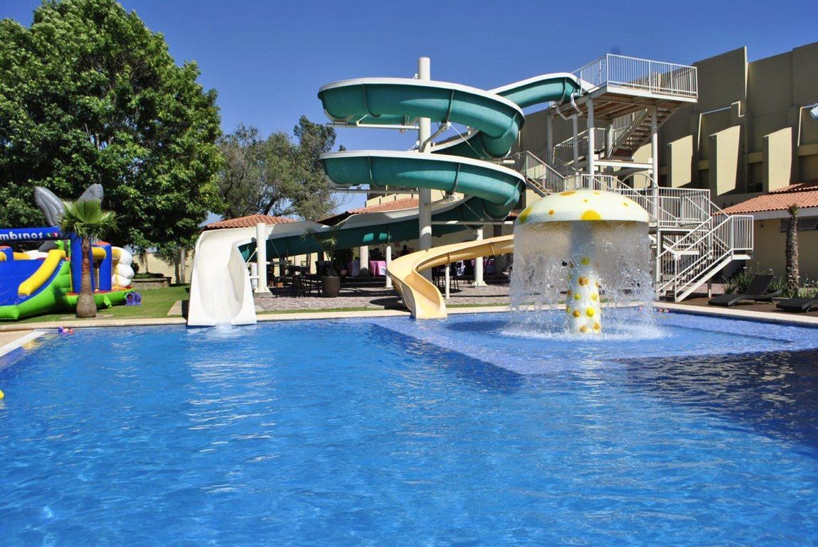 Piscina con toboganes acuáticos y fuente en forma de seta, al aire libre en un día soleado.