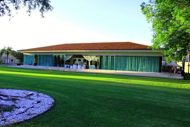 Edificio con tejado de tejas marrones y cortinas azul verdoso, situado en un césped verde con un árbol.