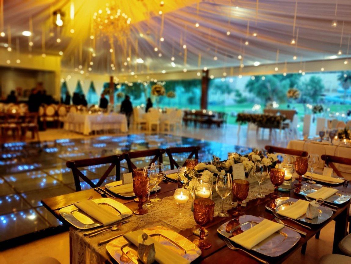 Recepción de boda con mesas preparadas para los invitados, pista de baile y guirnaldas de luces, en un espacio al aire libre.