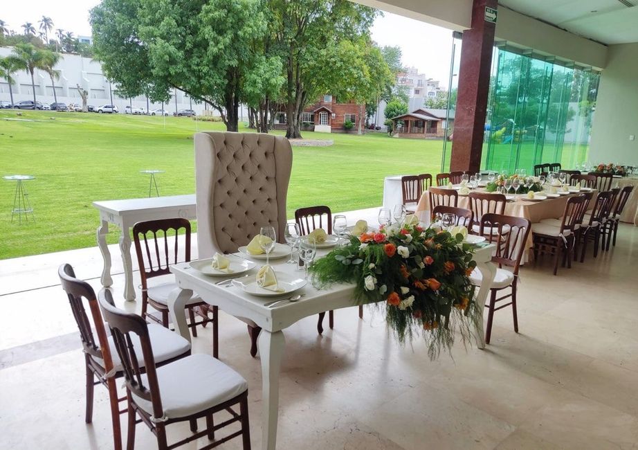 Mesas para la recepción de la boda dispuestas bajo un patio cubierto con vistas al césped; colores blanco, marrón y verde.