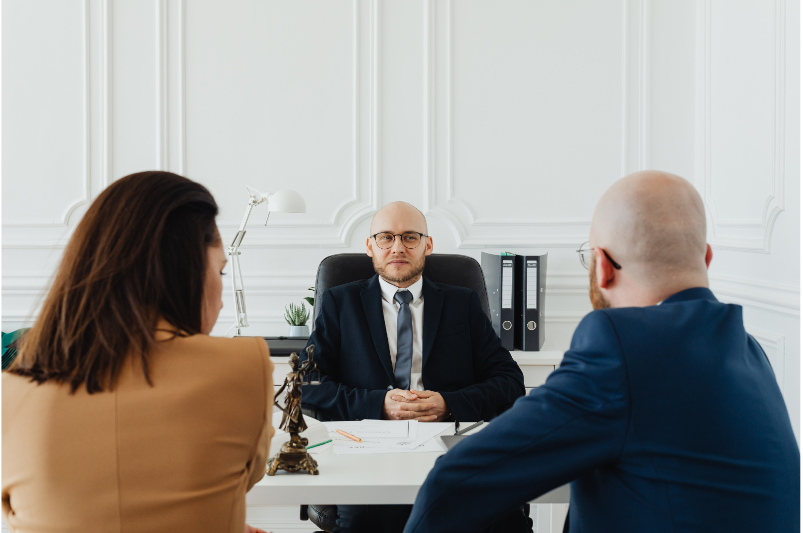 HR consulting firms can have a bald man in a suit sitting at a desk between a woman and a man; a legal setting.