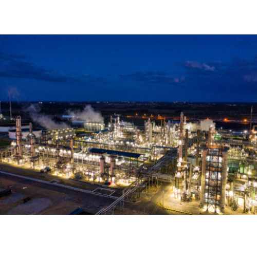 Nighttime aerial view of an industrial plant with lit towers, pipes, and smoke against a dark blue sky Houston.