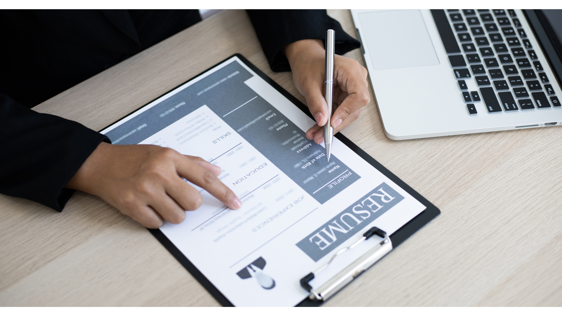 Person filling out a resume with a pen next to a laptop on a desk another example of fractional HR Leadership.