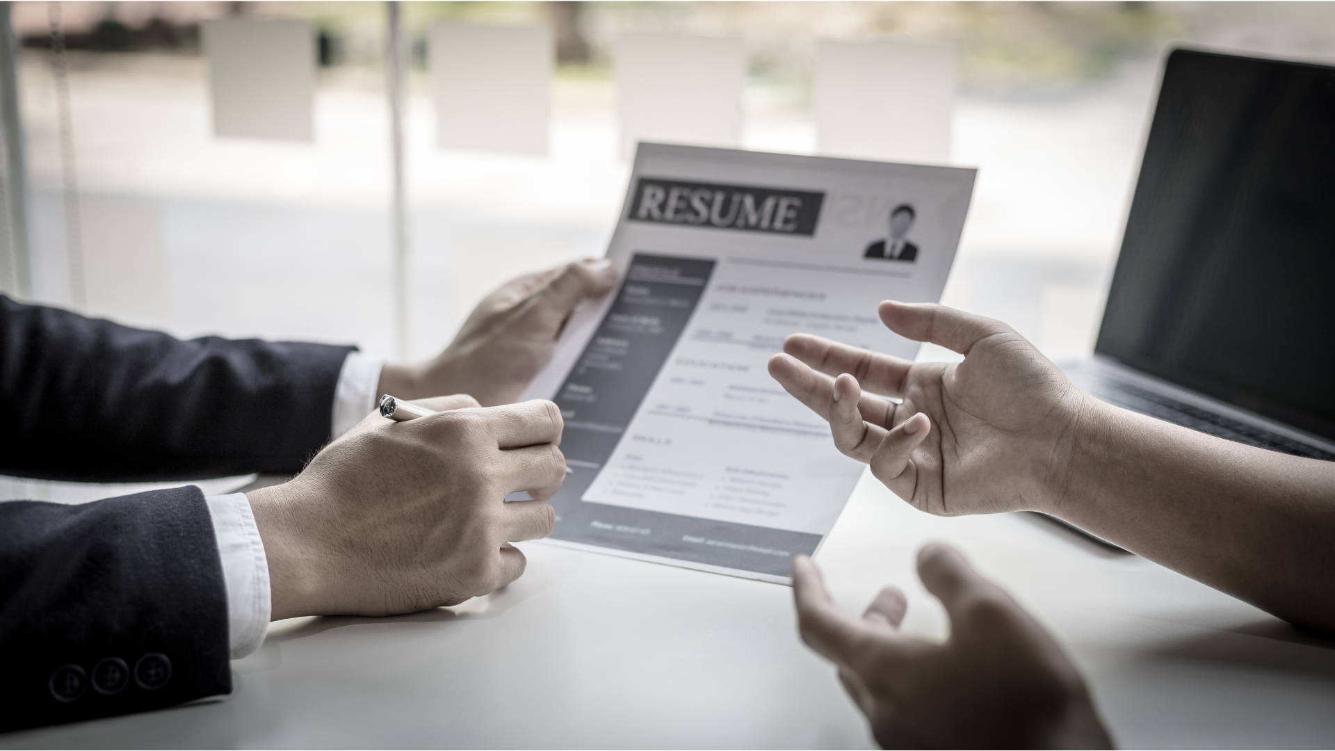 Two people reviewing a resume at a desk, one points, laptop in the background showing how fractional HR leadership can done.