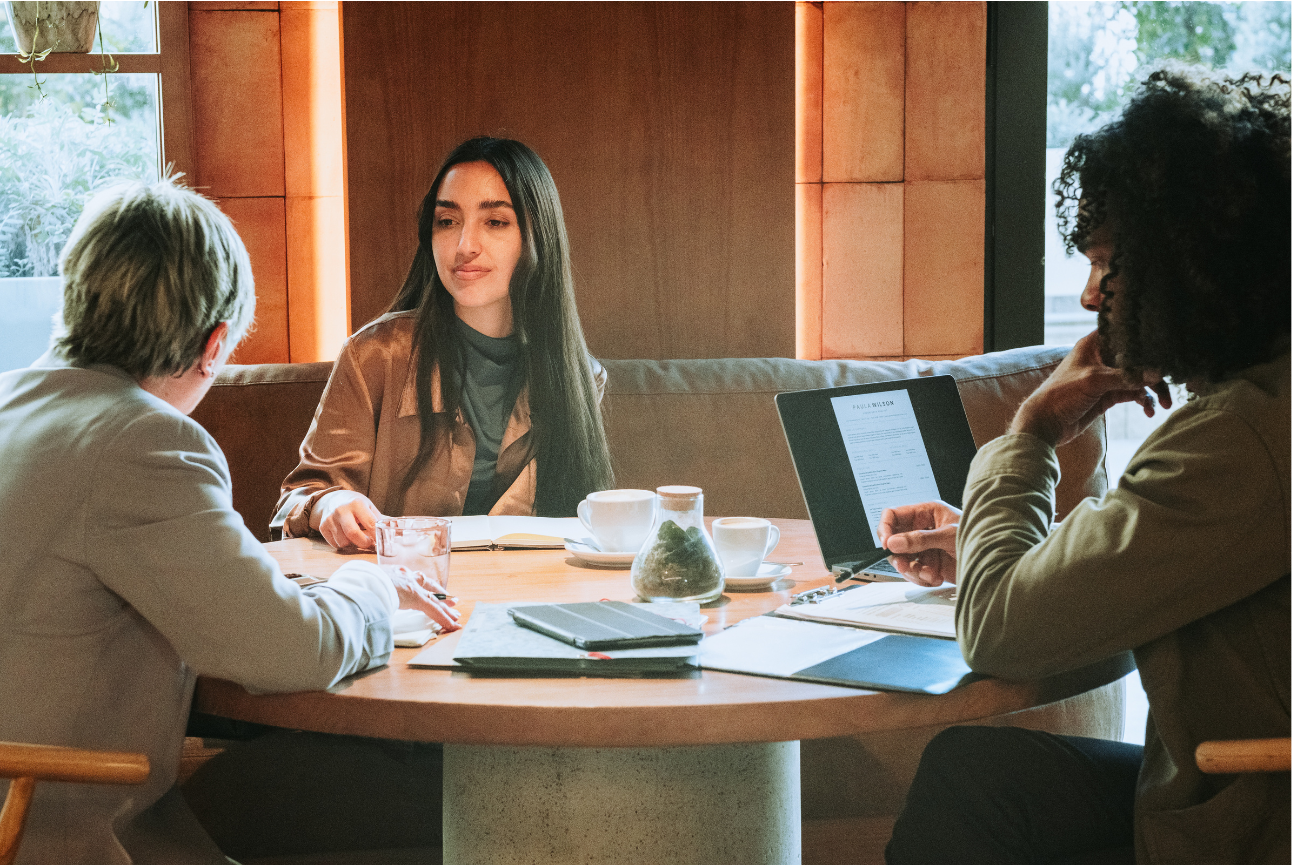 Three HR advisors are seated at a round table, discussing; a laptop is open.