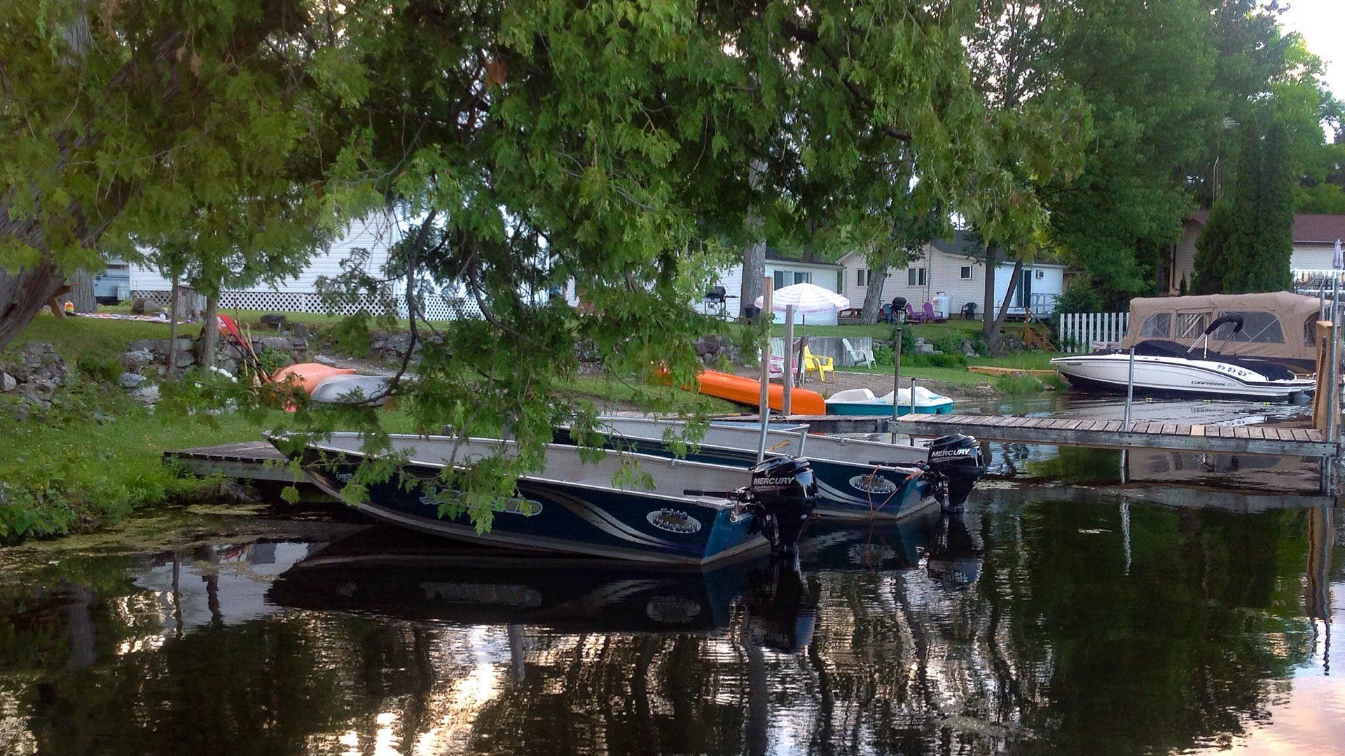 A row of boats are docked at a dock with a house in the background.