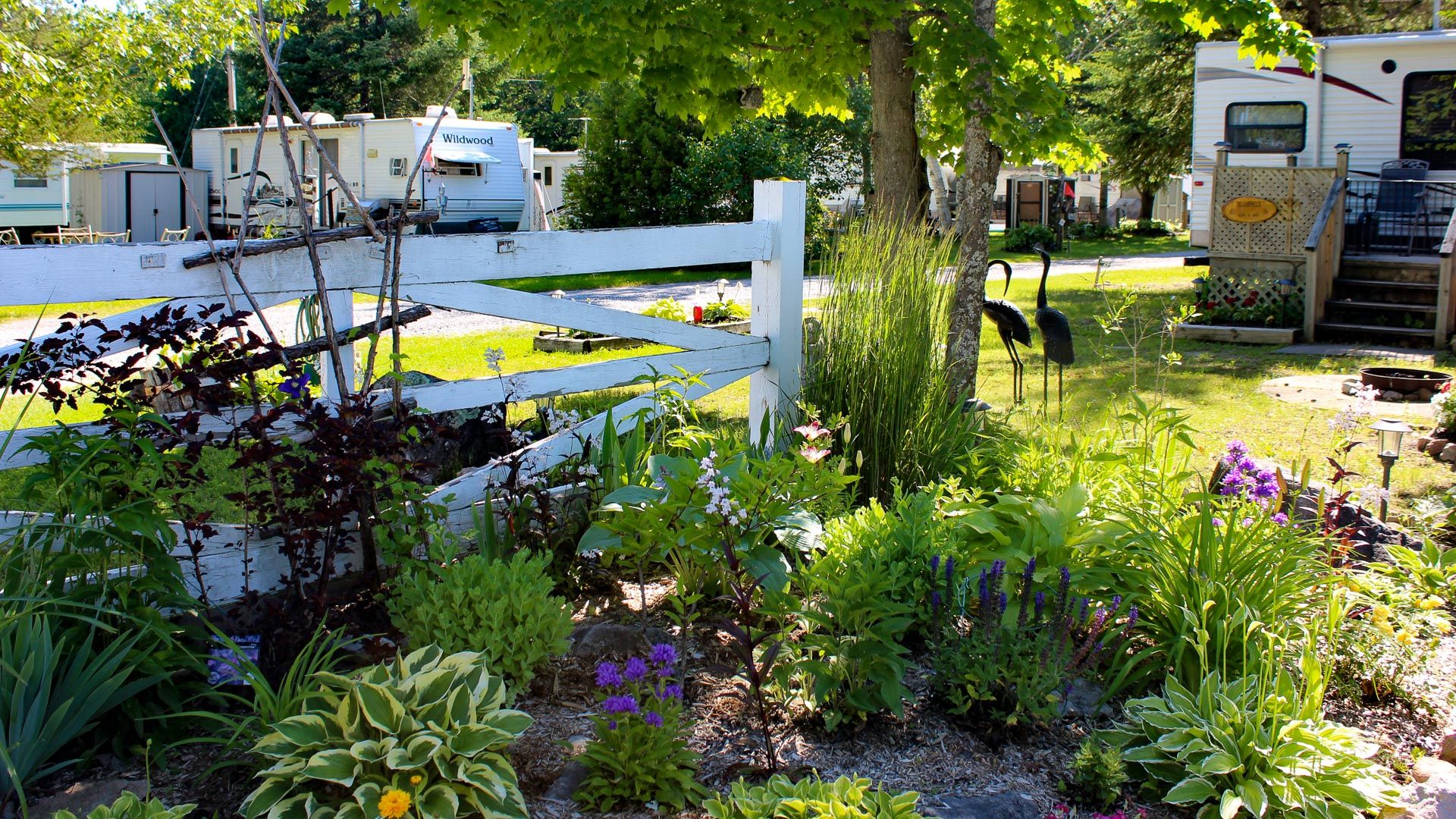 A white fence surrounds a garden with a rv parked in the background.