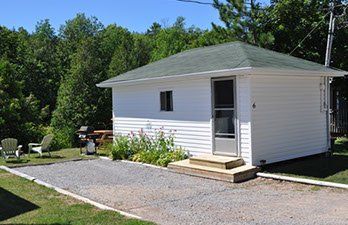 A small white house with a green roof is sitting in the middle of a grassy field.
