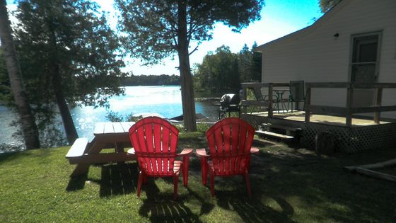 Two red lawn chairs sit in front of a picnic table overlooking a lake