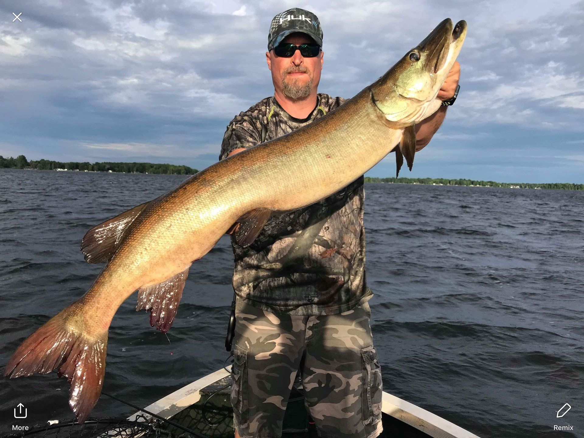 A man is standing in a boat holding a large fish.