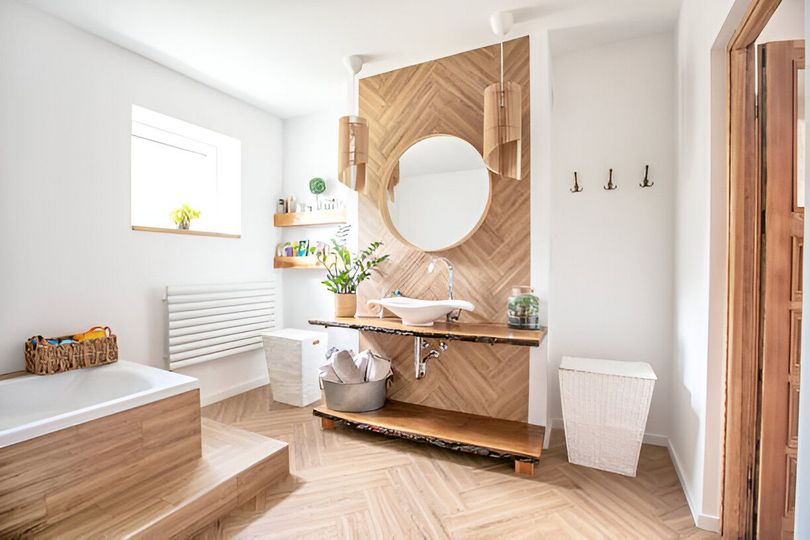 A bright bathroom with a wooden accent wall, sink, and floor, a bathtub, and white walls.