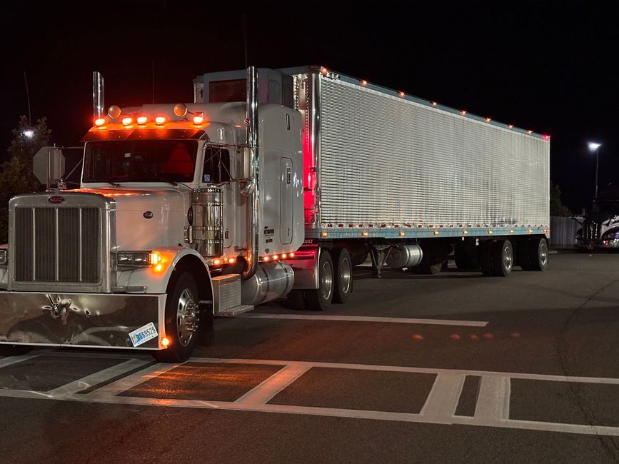 A white semi truck is driving down a dirt road in the desert.