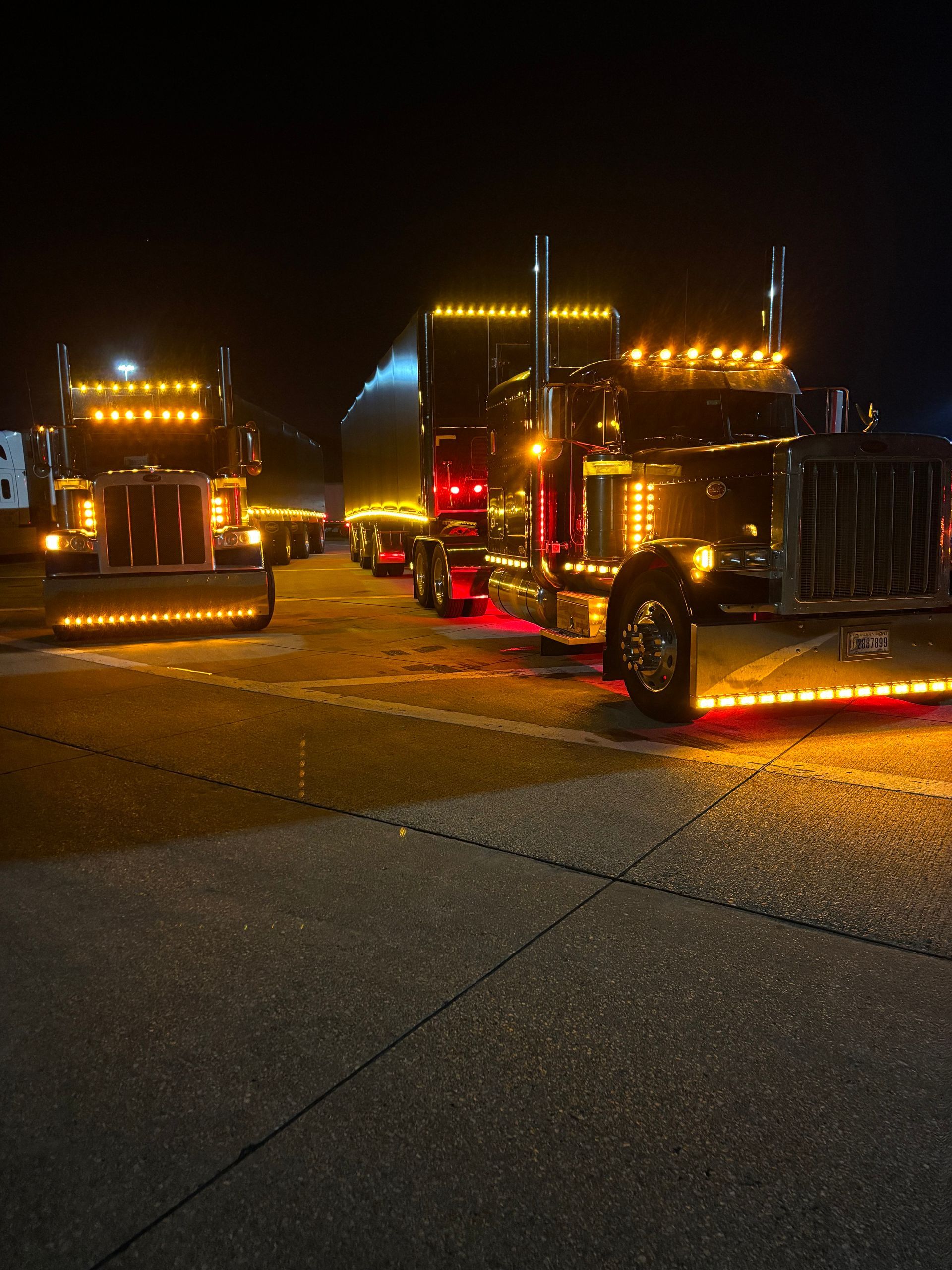 A row of semi trucks are parked in a parking lot at night