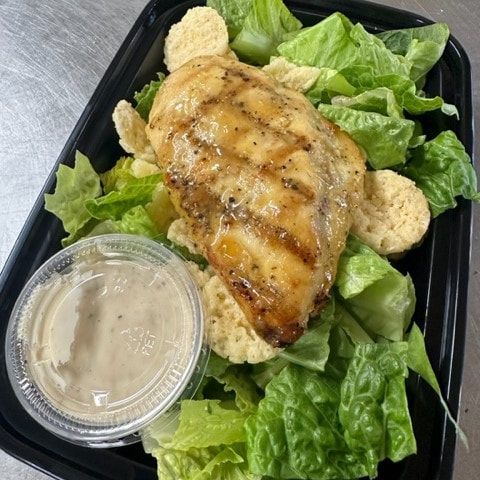 A caesar salad with grilled chicken , lettuce , croutons and dressing.