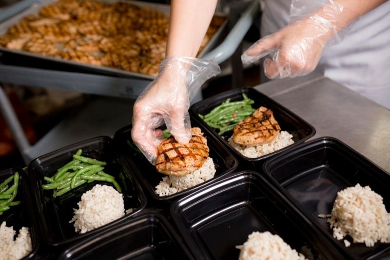 A person is preparing food in plastic containers in a kitchen.