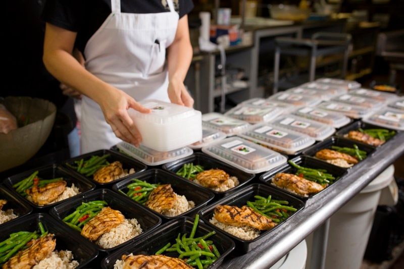 A woman is preparing food in plastic containers on a table.