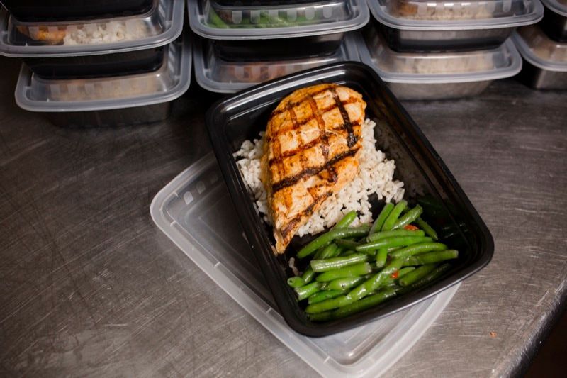 A container of food with rice and green beans on a table.