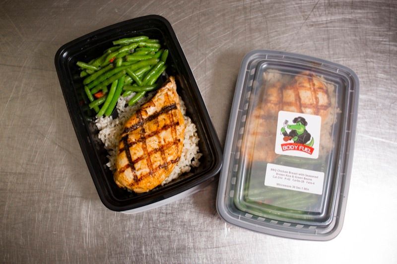 A plastic container filled with chicken , green beans , and rice.