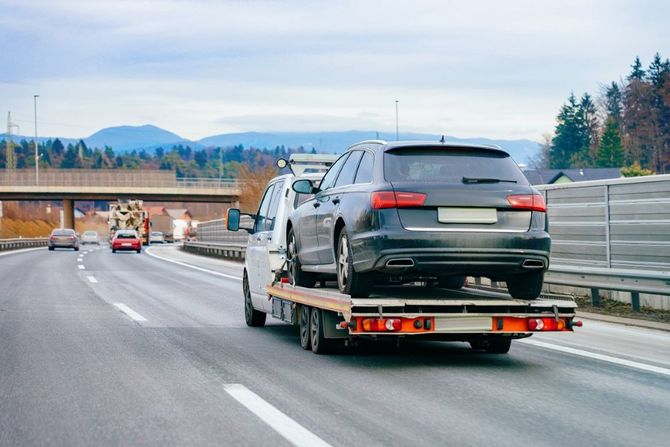 Tow truck hauling a black SUV on a highway, with mountains and trees in the distance