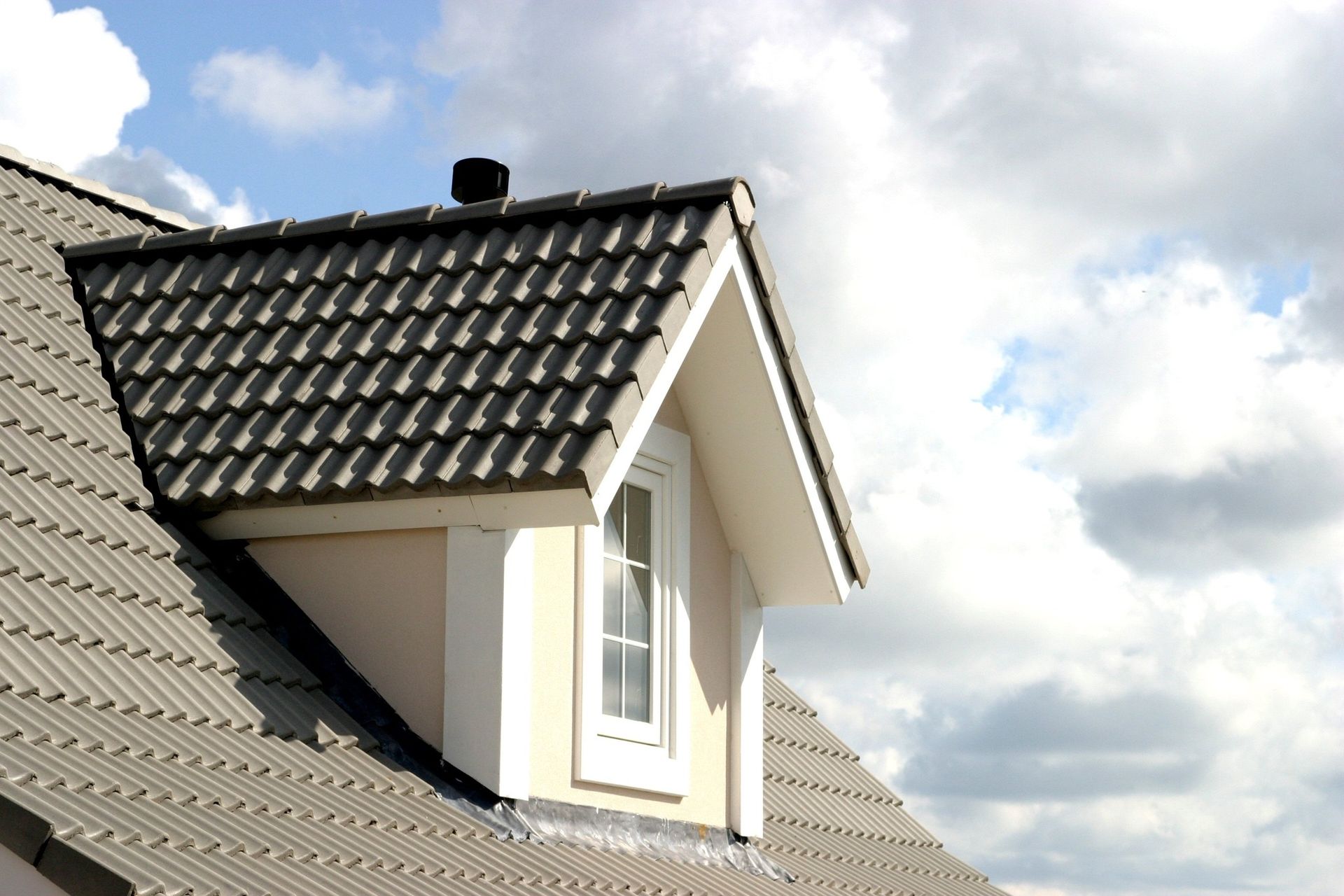 A roof with a window on it and a cloudy sky in the background