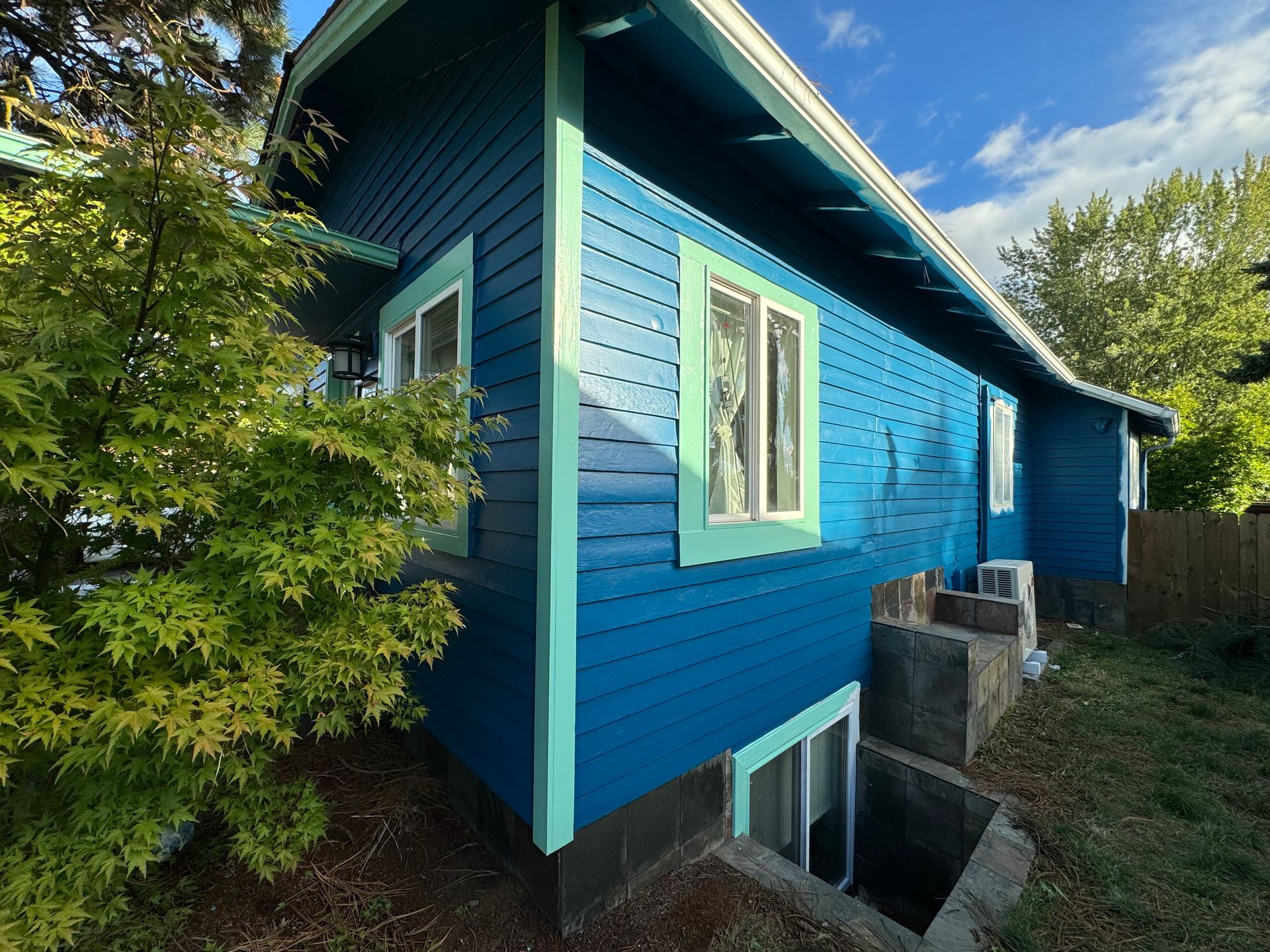 A blue house with green trim is surrounded by trees and grass.