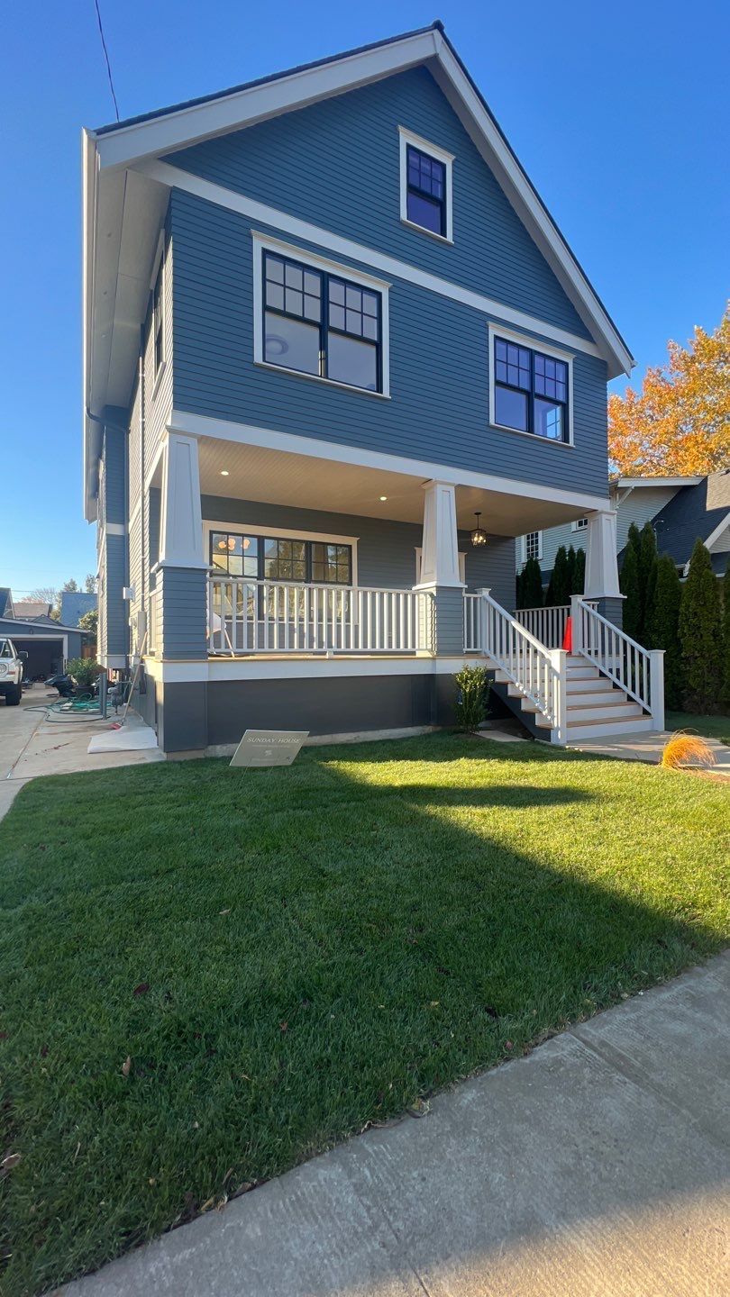 A large blue house with a white porch and stairs is sitting on top of a lush green lawn.