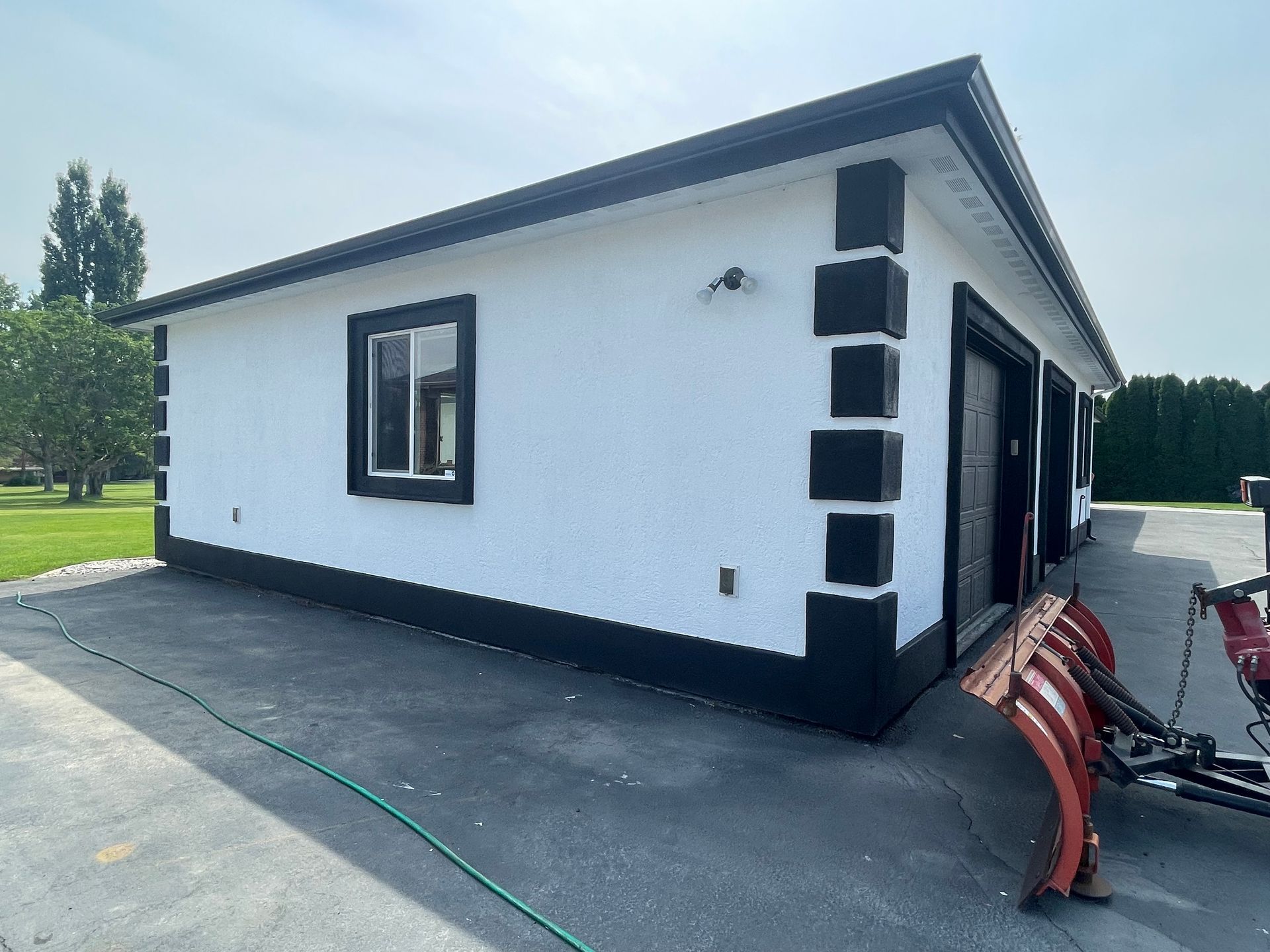 A white house with black trim and a snow plow in front of it.