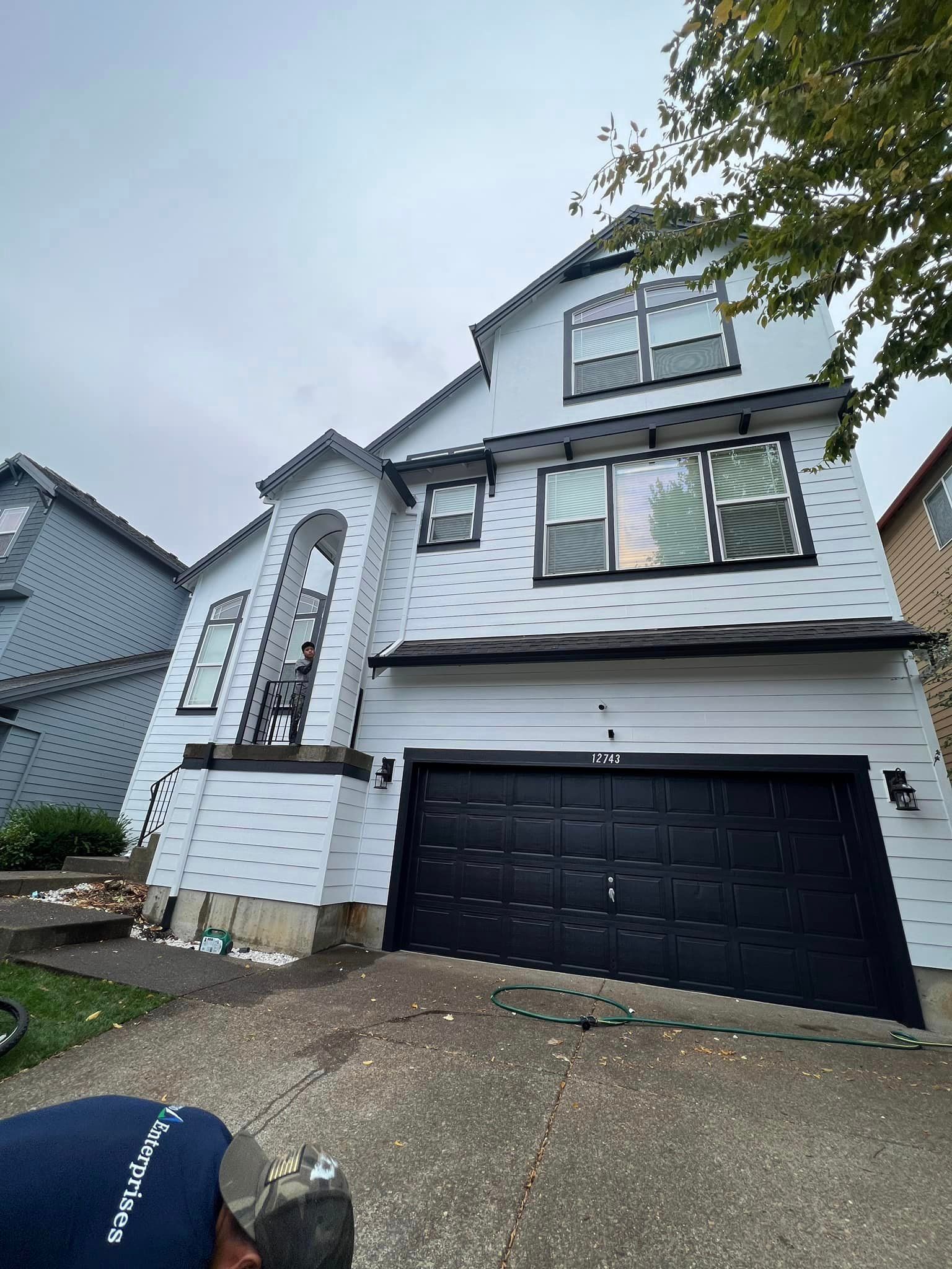 A man is standing in front of a white house with a black garage door.