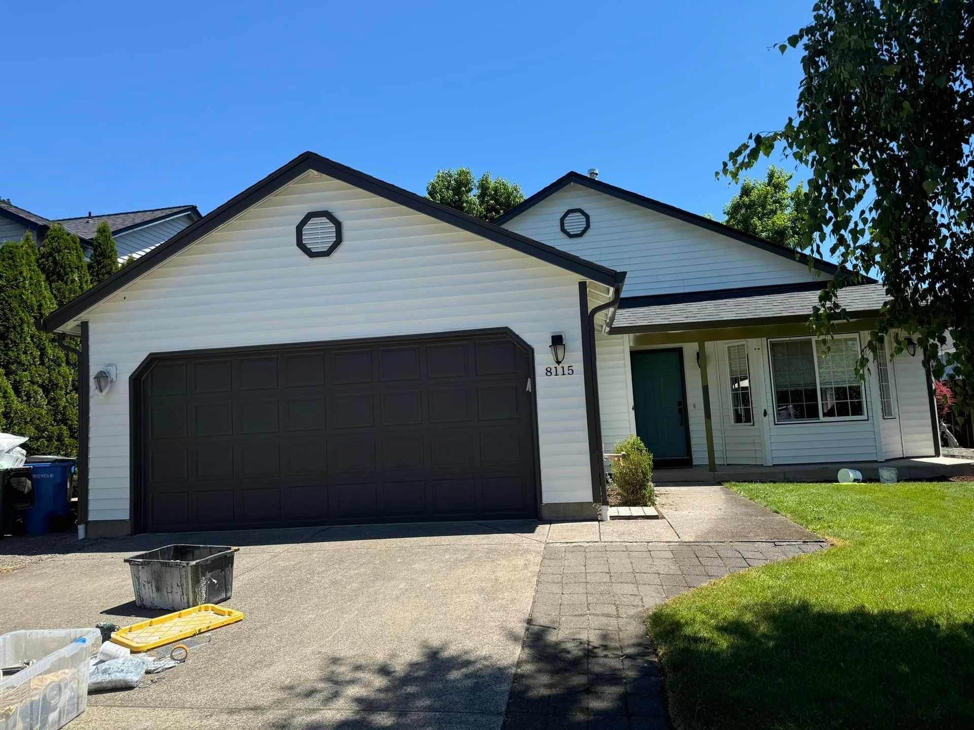 A white house with a black garage door and a blue sky in the background.
