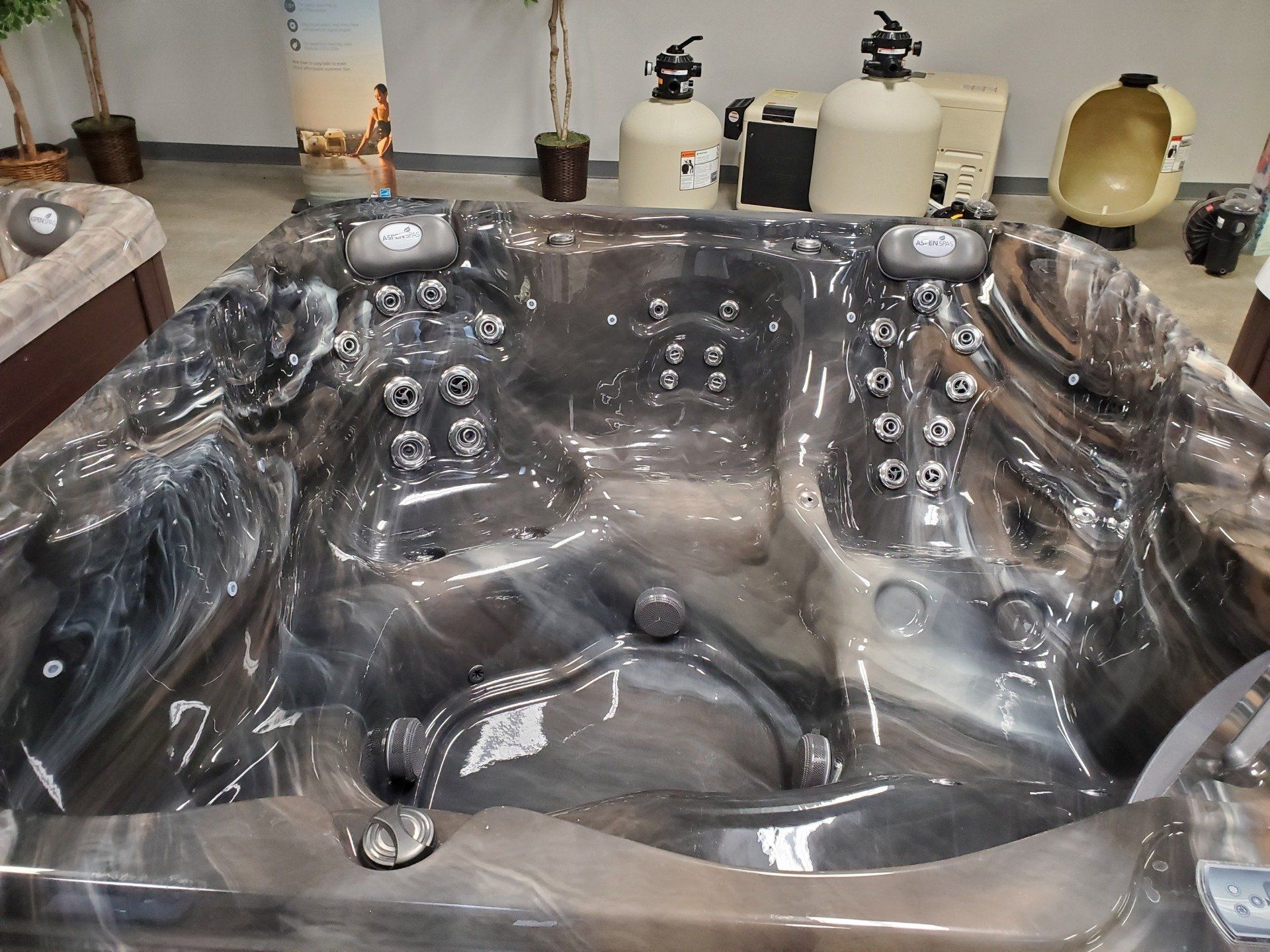 A large hot tub is sitting in a room next to a pool filter.