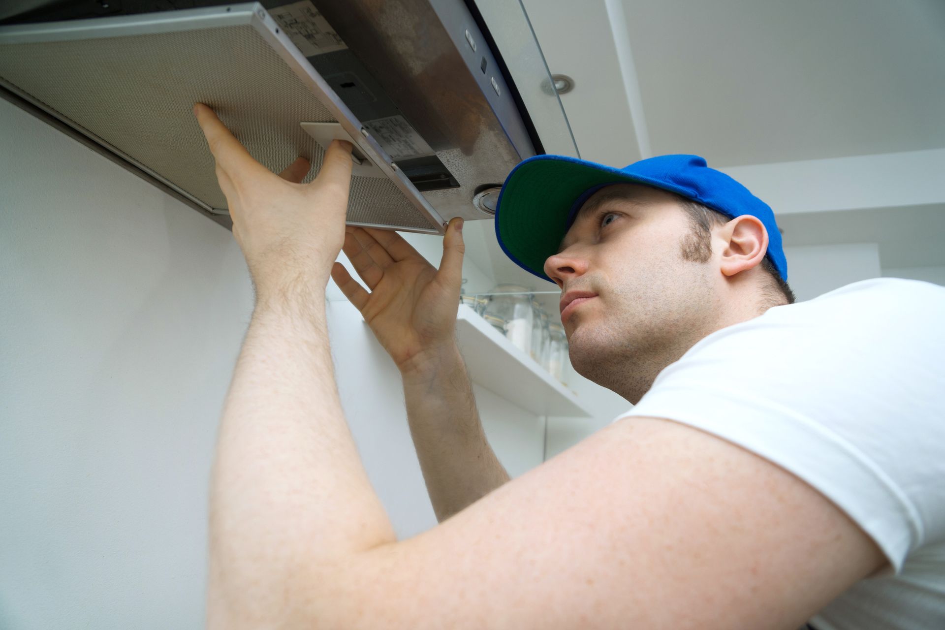 Man in blue cap installing a kitchen range hood filter.