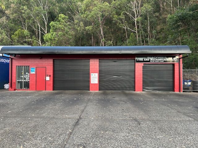 A Man is Working on a Car Tyre in a Garage — Blackwall Tyre Service & Mechanical Repairs In Blackwall, NSW