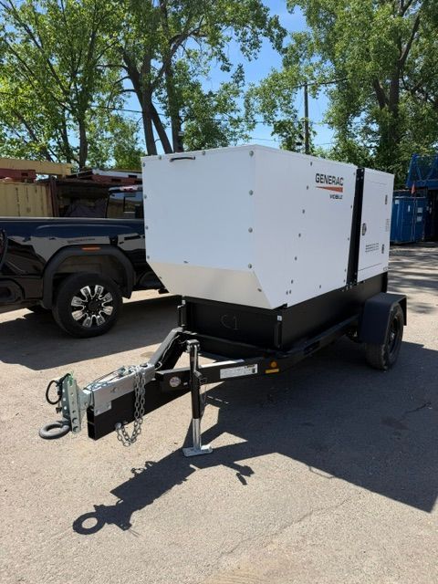 White generator trailer hitched behind a black pickup truck on a sunny roadside.