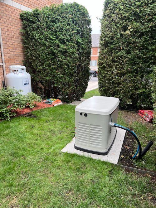 Un générateur est assis dans l'herbe à côté d'un réservoir de propane.