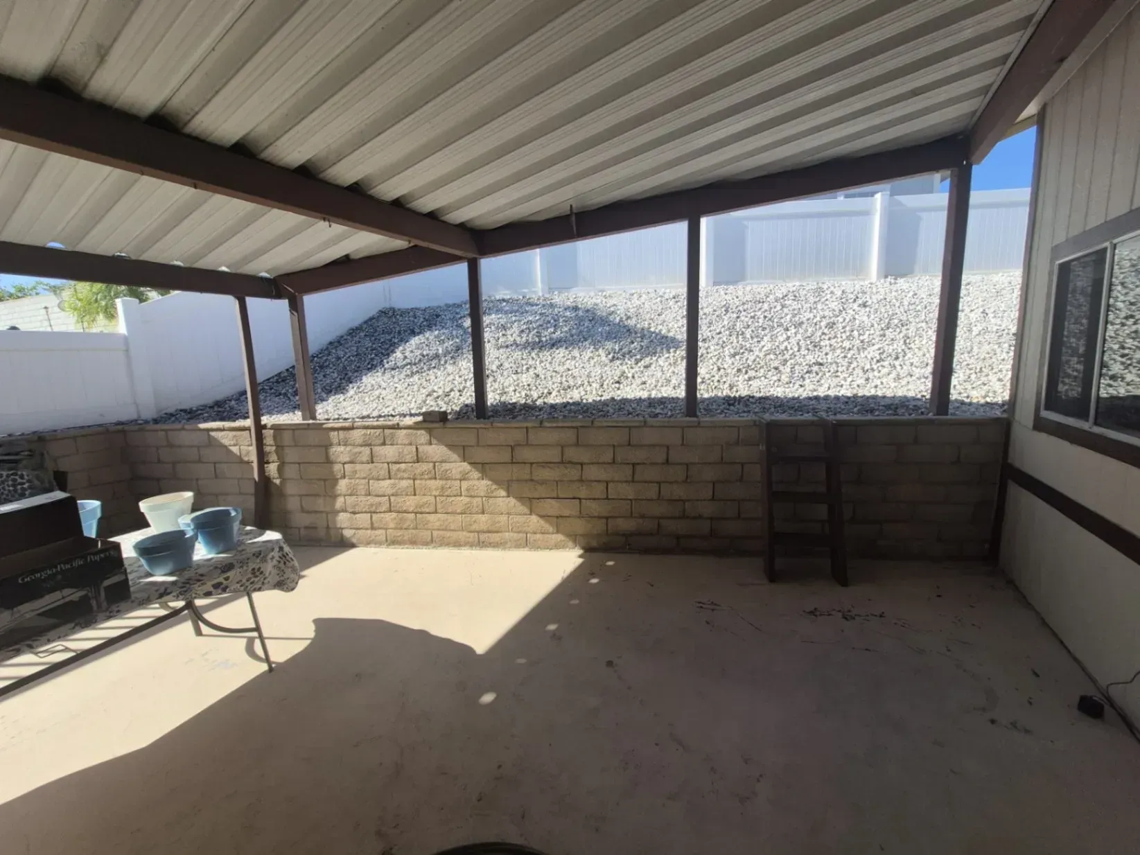 Covered patio with a concrete floor, block wall, and gravel hillside backdrop.
