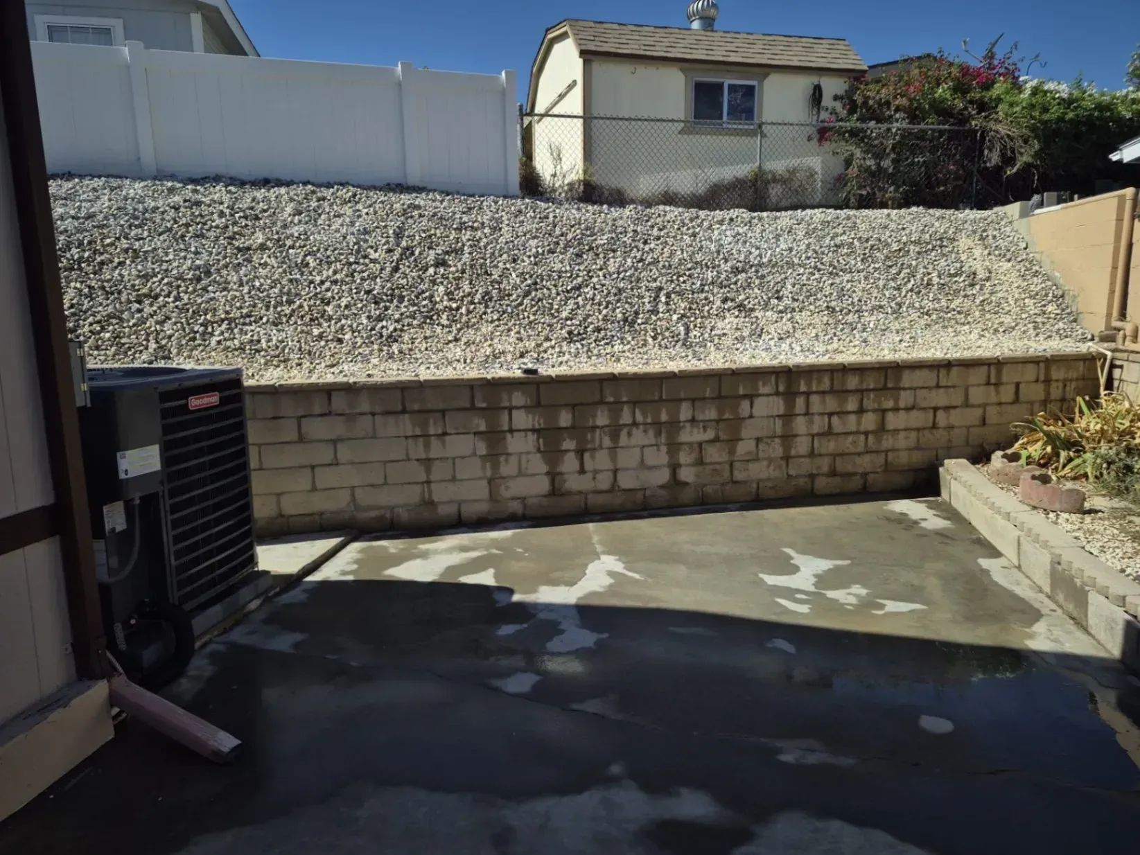 Concrete patio with a rock retaining wall and a white fence under a clear sky.