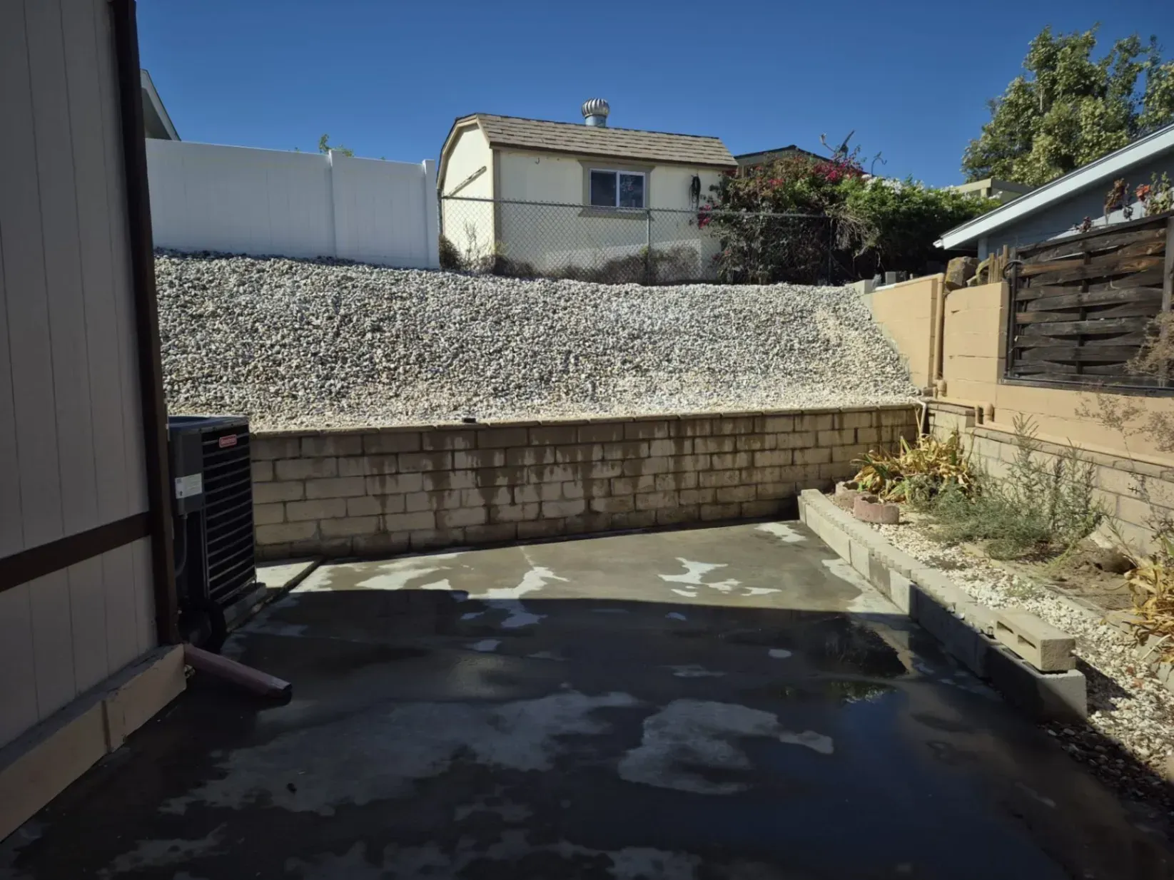 Backyard with concrete patio, retaining wall, and shed under a blue sky.